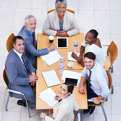 Five professionals in a meeting around a table with documents and digital devices.